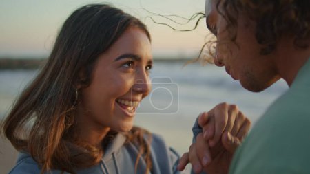 Closeup man kissing woman hands at evening coast. Happy teen lady face smiling toothy looking at boyfriend with love. Young pair expressing feelings dating at sunset ocean shoreline. Youth concept