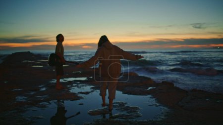 Photo for Couple silhouettes enjoying sundown ocean horizon. Relaxed young man playing guitar serenading at night beach. Woman stepping marine water at evening. Unrecognizable love pair spending time in nature - Royalty Free Image