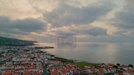 Panoramic seashore village view on cloudy sunset. Relaxing seaside landscape drone shot. Calm ocean surface reflecting light. Tranquil gloomy morning at coastal countryside. Scenic seascape concept