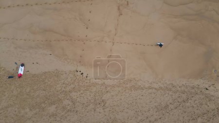 Surfboarder walking golden sand leaving footprints top view. Unrecognizable professional surfer stepping sandy seafront carrying surfboard. Unknown active person enjoying extreme hobby summer vacation