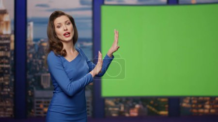Photo for Confident tv presenter hosting newscast showing on green screen at media channel studio close up. Beautiful smiling woman newscaster lighting current information on mockup monitor. Television industry - Royalty Free Image