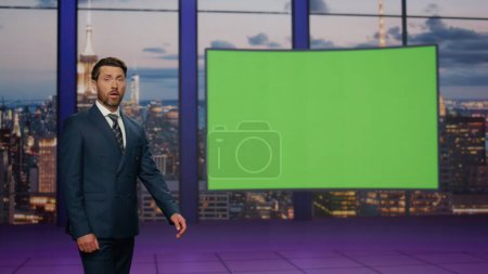 Confident newscast presenter talking daily news in modern tv studio with green screen. Bearded elegant newscaster showing image on mockup monitor. Television newsroom channel with professional anchor.