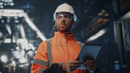 Serious factory supervisor looking at manufacturing process making notes in tablet close up. Skilled technician analyzing technology at production warehouse. Uniformed specialist using pad computer.