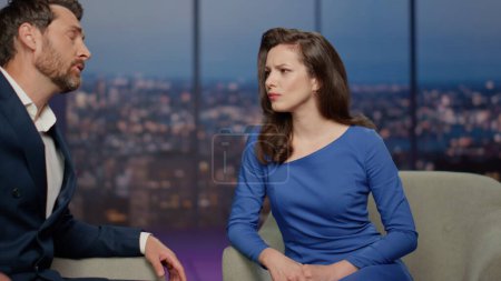 Two tv show people discussing global world problems in air studio close up. Sad bearded man expert complaining on economics crisis to beautiful woman host. Upset couple presenters talking in program.