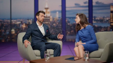 Sad guest tv show sharing life troubles with woman host in modern studio. Upset bearded businessman discussing personal problem with anchorwoman on television entertainment program. Broadcast concept.