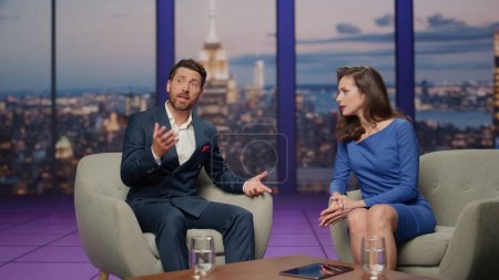 Two presenter talking tv show sitting comfortable armchairs studio. Positive bearded man telling news thoughts to pretty anchorwoman. Couple television workers hosting entertainment program on channel