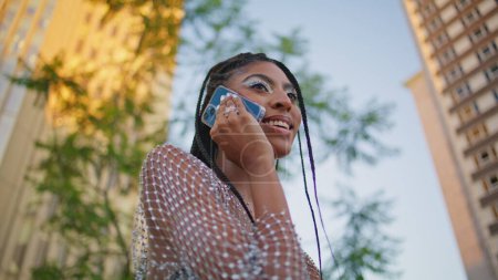 dreadlocks fille détendue parlant téléphone mobile à proximité banc de la ville. Une femme afro-américaine branchée termine son coup de fil au centre-ville d'été. Femme attrayante utilisant la cellule pour la communication dans la rue