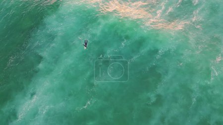 Vista aérea surfista nadando en el océano fin de semana de verano. Top tiro irreconocible surfboarder acostado a bordo esperando ola perfecta. Hermosa turquesa agua de mar balanceo persona desconocida en cámara súper lenta.