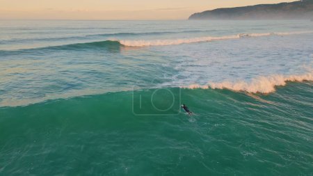 Luftbild Unbekannter Surfboarder genießt Meereswellen auf Surfbrett liegend. Extreme Surfer Skateboarding Hobby in türkisfarbener See Zeitlupe. Schaumig stürmisches Wasser plätschert am tropischen Strand