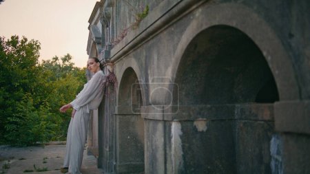 Vogue-Model posiert in weißem Anzug im verlassenen Palast. Wunderschöne stilvolle Frau lehnt an Steinmauer alten Burg im Freien. Ernsthafte selbstbewusste Mädchen suchen Kamera stehen alte Festung