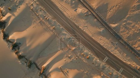 Top view empty sand road over summer dunes nature. Aerial asphalt highway stretching between desert. Overhead sandy trail path. Dirty landscape with brown offroad. Adventure and journey concept