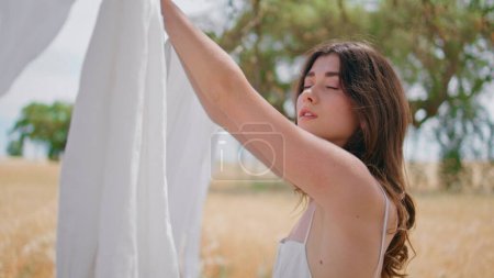 Young housewife hanging laundry at sun beams rural nature closeup. Portrait sensual lady looking at camera posing at countryside. Brunette woman putting clean white linen on rope enjoying washing day