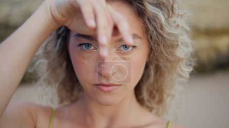 Closeup woman dancer moving hands smoothly on sand beach. Curly young performer with magnetic gaze looking camera making graceful arms movements. Portrait of serious girl dancing on summer nature.