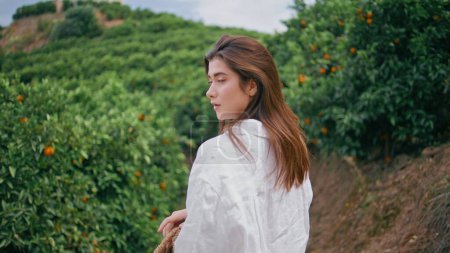 Seductive model gazing over shoulder in green slopes portrait. Proud calm woman looking distance posing in citrus trees greenery hills nature zoom on. Lady standing on tangerine plantation background