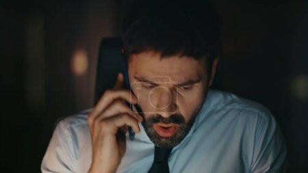 Concerned manager arguing at telephone call sitting office late evening close up. Frustrated nervous businessman finish phone conversation at workplace. Stressed ceo dissatisfied by communication.
