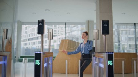 Dissatisfied woman enter office turnstile talking smartphone. Hurrying girl manager cannot pass security control expressing displeasure. Worried woman calling standing near closed electronic gates.