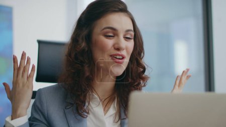 Emotional employee video calling at office laptop looking web camera with smile close up. Excited beautiful woman manager talking gesturing at online meeting. Successful businesswoman feeling happy.