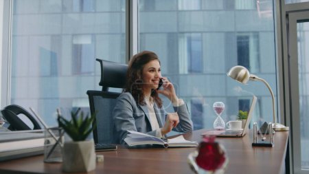 Girl consultant talking phone sitting luxury office close up. Elegant successful woman manager consulting client working at laptop on desk. Smiling businesswoman enjoy pleasant telephone conversation.
