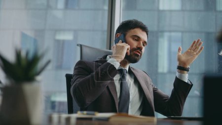 Rich business owner calling phone rejoicing success sitting office close up. Happy confident businessman talking smartphone with smile at workplace. Handsome bearded ceo manager speaking cellphone.
