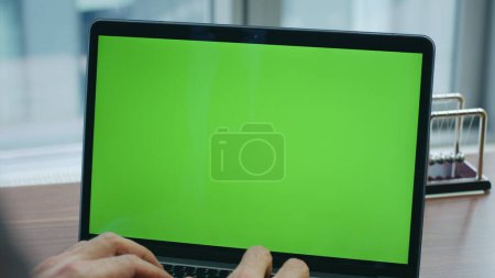 Unrecognizable manager working green screen laptop standing on wooden office table close up. Man hands typing on computer keyboard at luxury workplace. Unknown worker writing report at mockup notebook