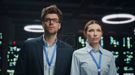 IT administrators couple working in network data storage server room closeup. Serious technicians man woman looking distance at modular datacenter. Engineers colleagues in operative modern cabinet 