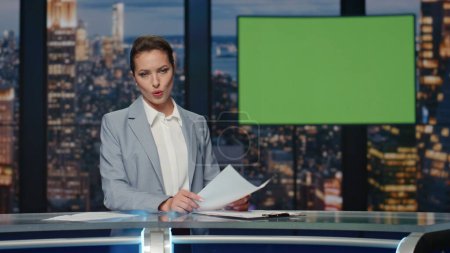 Presenter showing mockup screen reporting breaking news in tv channel studio. Woman newsreader in elegant suit talking about daily events standing at chroma key monitor. Television industry concept