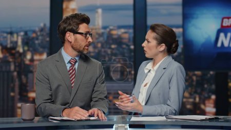 Serious anchors broadcasting news at evening multimedia channel closeup. Confident man woman newsreaders discussing daily information in late television studio. Two presenters reporting newscast