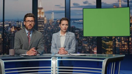 Two presenters broadcasting news at mockup television media channel closeup. Happy anchors hosting newscast standing chromakey tv studio. Charismatic couple newscasters talking collaborating in air