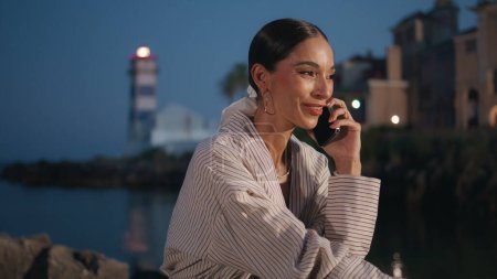 Laughing woman talking cellphone sitting embankment on vacation close up. Excited businesswoman calling phone relaxing on coastal city at twilight. Happy relaxed girl enjoy conversation on weekend.