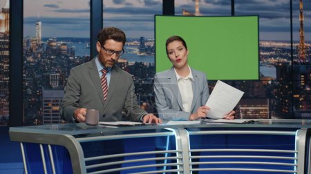 Photo for Cheerful anchors smiling in mockup studio evening television channel closeup. Friendly couple newsreaders reporting breaking news lighting information. Happy anchorwoman talking at greenscreen place - Royalty Free Image