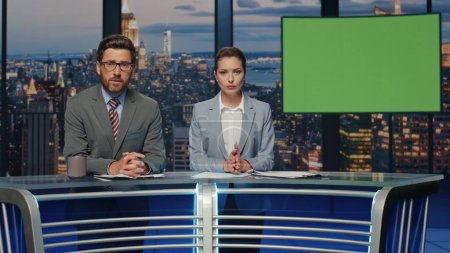 Serious presenters talking greenscreen news standing evening tv studio closeup. Couple professional anchors hosting newscast on modern channel. Two newsreaders lighting daily events in television air 