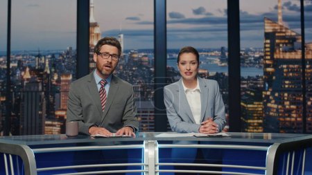 Presenters broadcasting breaking news at late studio closeup. Friendly couple professional newscasters working on tv studio stage talking to viewers. Elegant smiling hosts speaking at evening newscast