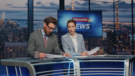Presenters lighting breaking news in late evening tv studio closeup. Confident newsreaders hosting newscast at modern multimedia channel. Elegant anchors presenting daily politics event discussing