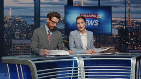 Photo for Confident anchors announcing news at evening modern studio closeup. Professional television presenters talk broadcasting in newsroom together. Elegant couple hosts lighting daily world events newscast - Royalty Free Image