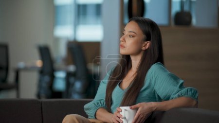Relaxed ceo drinking tea enjoying break in office closeup. Calm person dreaming thinking in cozy place. Satisfied woman sipping cappuccino with pleasure. Asian boss looking away delighting working day