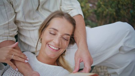 Smiling girlfriend enjoying book with unknown man at bench closeup. Handsome unshaven boyfriend holding novel reading aloud for loving woman. Brunette macho spending time with lady. Love concept