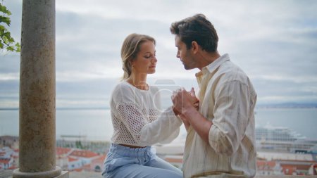 Verliebtes Paar küsst Stadtbild-Terrassen-Date Nahaufnahme. Zärtliche Männerfrau hält Händchen und streichelt sich beim mediterranen Städtetreffen. Romantische Verliebte fühlen sich auf dem Balkon am Meer wohl