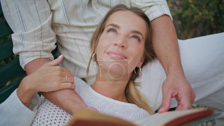 Serene woman laying boyfriend knees relaxing at bench park closeup. Unrecognizable man hands holding book reading at fresh air nature. Tender lovers touching caressing enjoying romantic date at garden