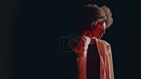Elegante Dame dreht Kamera und posiert in rosa Licht. Modelsilhouette auf dunklem Hintergrund. Lockige attraktive Frau berühren Frisur suchen Kamera. Sexy afrikanisch amerikanisch mit make-up vor party.