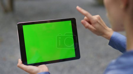 Photo for Hand using green tablet outdoors closeup. Girl finger swiping chroma key pad watching online webinar in social media in blurred background. Unrecognized woman ceo touching screen working remotely. - Royalty Free Image