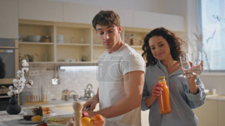 Feliz par de comida de cocina en la cocina cómoda de cerca. Pareja romántica disfrutar de la mañana familiar preparando sabroso desayuno. Hombre guapo rebanando manzana fresca mientras la mujer toma vasos para el jugo de naranja.