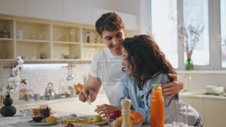 Romantic lovers eating breakfast on cozy kitchen leaning at countertop close up. Happy smiling husband feeding pretty woman with apple slice. Cheerful relaxed couple enjoy family weekend at home.