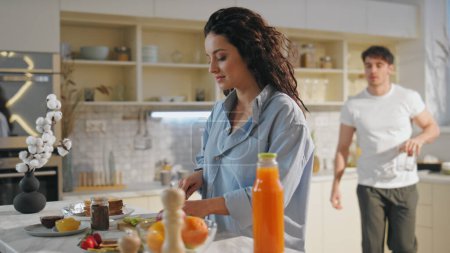 Young pair preparing breakfast together at home close up. Beautiful woman slicing fresh apple at cozy kitchen. Smiling handsome boyfriend taking glasses for orange juice. Happy marriage concept. 
