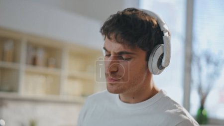 Man preparing breakfast in earphones dancing at cozy kitchen close up. Attractive young guy singing favorite song from headphones cooking at home. Joyful happy melomaniac listening music at morning.
