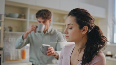 Couple breakfast hurrying work at modern apartment kitchen close up. Loving husband giving coffee cup to beautiful woman sitting with tablet computer. Busy man kissing woman cheek for goodbye at home.