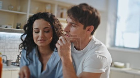 Loving couple standing kitchen relaxing feeling happiness close up. Happy smiling married pair enjoy family morning together. Handsome husband eating fruits talking with carefree beautiful wife.