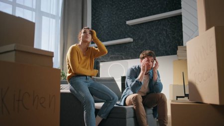 New homeowners sitting tired of moving in purchased house. Exhausted married couple rest from relocation near cardboard boxes. Fatigued young spouses relaxing on couch rent apartment. Property owners.