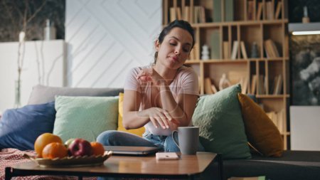 Tired woman drinking coffee after remote laptop work late evening. Serious young lady sitting comfortable couch modern living room with cup hot tea. Overworked girl freelancer relaxing after hard day.