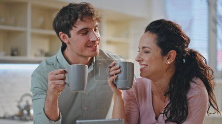 Photo for Married couple drinking coffee laughing talking together at home kitchen interior close up. Happy two people in love enjoy morning beverage looking tablet screen. Cheerful spouses having breakfast. - Royalty Free Image