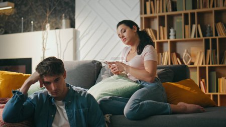 Couple sitting couch with gadgets at weekend evening close up. Relaxed girlfriend surfing social media on smartphone looking boyfriend working laptop leaning at sofa. Carefree family leisure concept.
